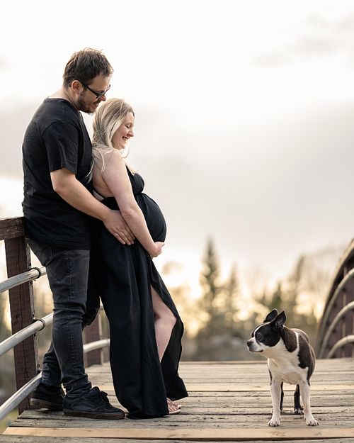 Expecting couple sharing a moment with their dog on a bridge.
