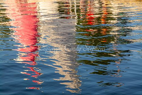Colorful sailboats are reflected in water at sunset